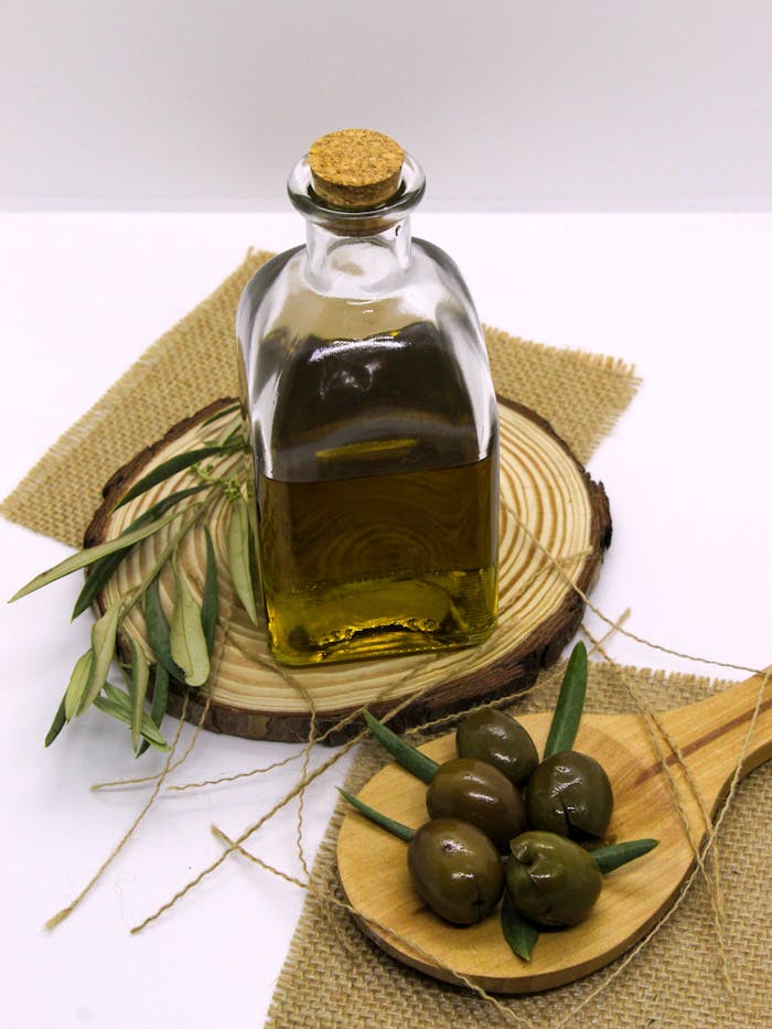 Artistic shot of olive oil bottle with olives, leaves, and wood elements in a rustic setup.