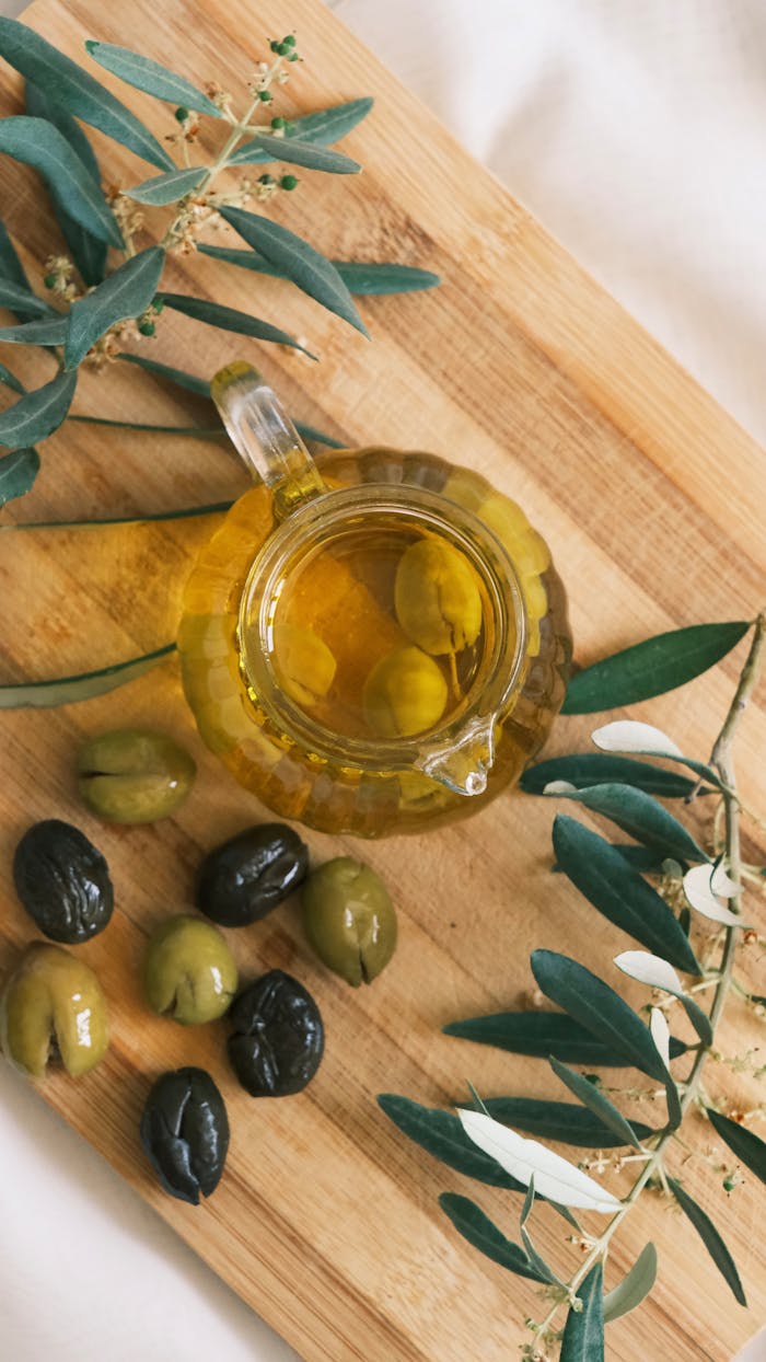 A top view of a cruet with olive oil and olives on a wooden cutting board.